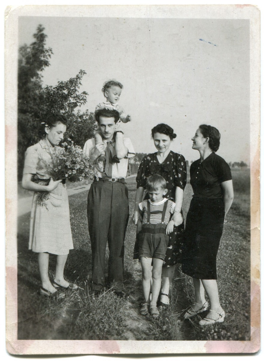 3 kobiety i mężczyzna z dzieckiem na ramionach, stojący na łące. Obok niego chłopiec około 6-7 lat