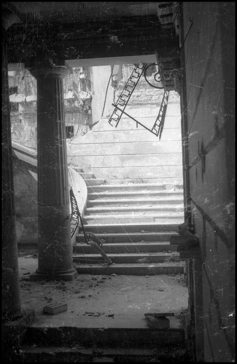 Wnętrze zburzonego pałacu: cegły leżące na korytarzu, zniszczone schody z odłamanymi poręczami 
