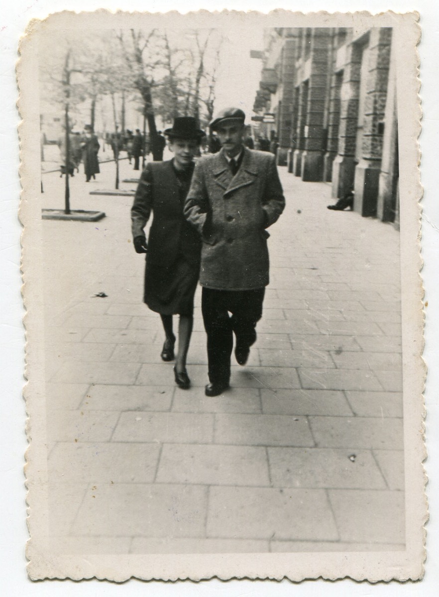 Para młodych ludzi, idących pod rękę szerokim chodnikiem. Z lewej kobieta, z prawej mężczyzna 