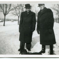 Dwaj młodzi mężczyźni w zimowych płaszczach na spacerze z psem. Ziemia pokryta śniegiem