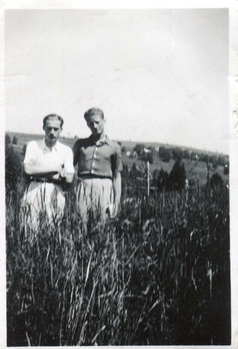 Dwaj mężczyźni około 20 lat, stojący obok siebie w trawie do kolan. W tle niewysokie góry