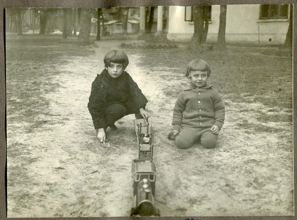 Dwaj chłopcy około 7 i 5 lat na ogrodowej ścieżce z zabawką-kolejką, poważnie patrzący w obiektyw