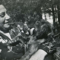 Kobieta na wiklinowym fotelu w ogrodzie, z uśmiechem patrząca na psa, którego trzyma na kolanach