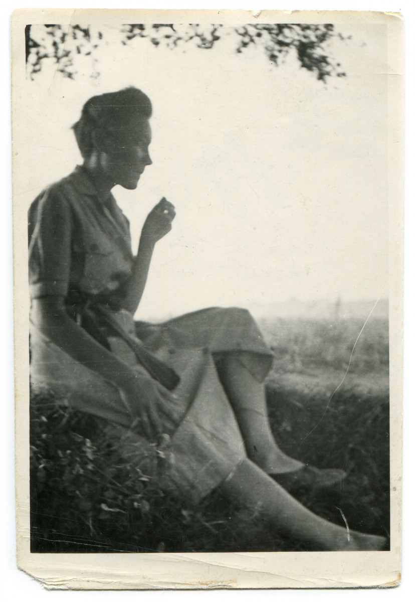 Ukazana z profilu dziewczyna w sukience, siedząca na trawie pod drzewem