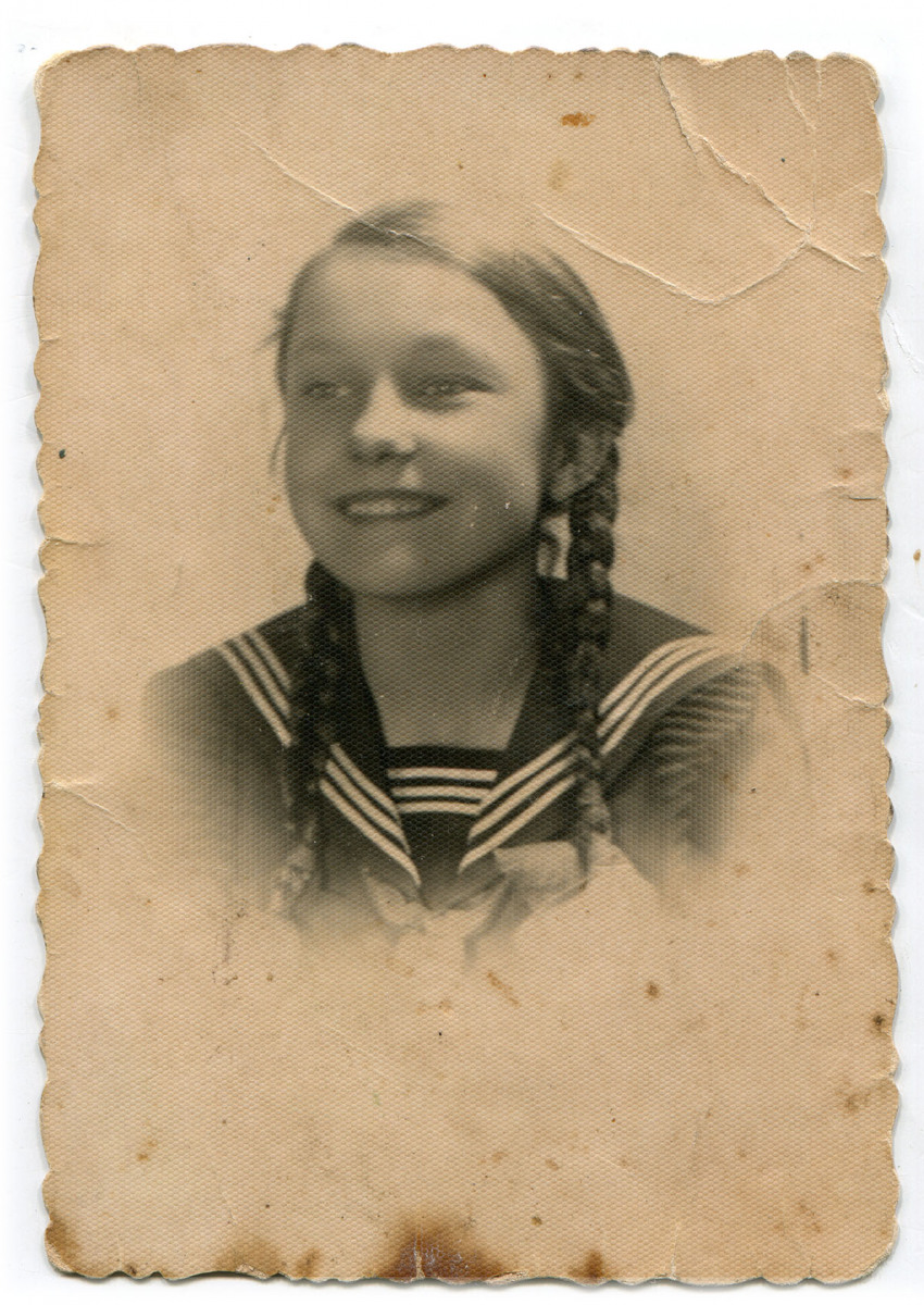 Legitymacyjne zdjęcie uśmiechniętej dziewczynki z warkoczami, ubranej w marynarską bluzkę