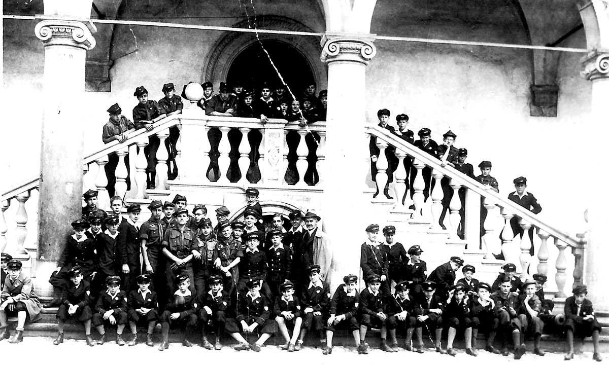 Kilkudziesięciu chłopców w mundurkach szkolnych i harcerskich na schodach z renesansową balustradą
