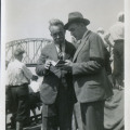 Dwaj mężczyźni, zaglądający razem do notesu. Za nimi tyłem chłopcy, patrzący na most w tle