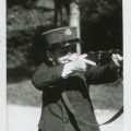 Chłopiec około 12 lat w mundurku szkolnym i kepi z emblematem szkoły, mierzący w prawo z karabinka