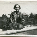 Kobieta z kotem w ręku za kamienną balustradą, na której widać 2 psy – jeden leży, drugi siedzi obok