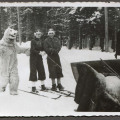 Człowiek w stroju białego niedźwiedzia i dwoje młodych narciarzy przy saniach widocznych z prawej