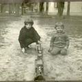 Dwaj chłopcy około 7 i 5 lat na ogrodowej ścieżce z zabawką-kolejką, poważnie patrzący w obiektyw