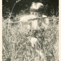 Chłopiec około 7 lat, klęczący na jedno kolano w wysokiej trawie i celujący z łuku-zabawki na wprost