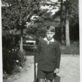 Chłopiec około 12 lat w mundurku szkolnym, stoi w parku z karabinkiem w prawej i kepi w lewej ręce